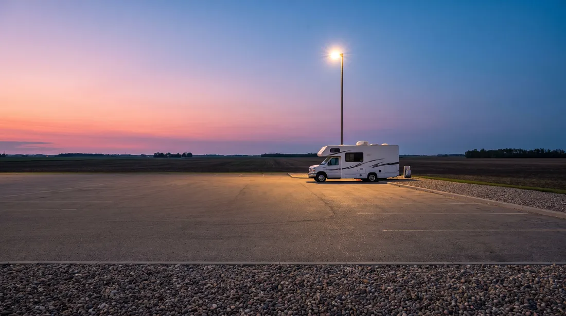 White motorhome alone on a paved lot at dusk